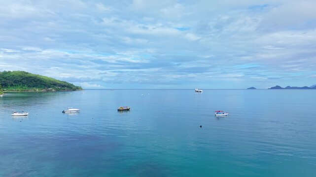 Cinematic drone passing above a docked local fishing boat on the tranquil, crystal-clear turquoise waters of Anse La Mouche, Mahe, Seychelles 30fps
