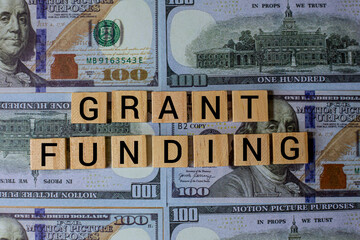 Fototapeta premium Grant Funding Concept with Wooden Letter Tiles on Dollar Bills Background Representing Finance Investment Support