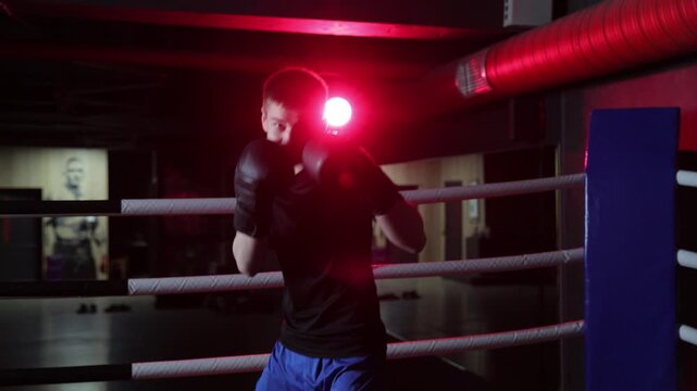 Determined young boxer training in a dark ring