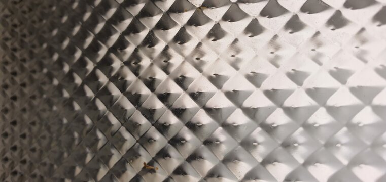 Abstract textured glass surface with geometric diamond pattern and soft monochrome reflections. Frosted translucent material creates elegant optical distortion and modern architectural texture