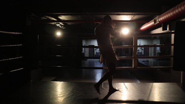 Silhouette of a fighter training alone in a dark boxing ring