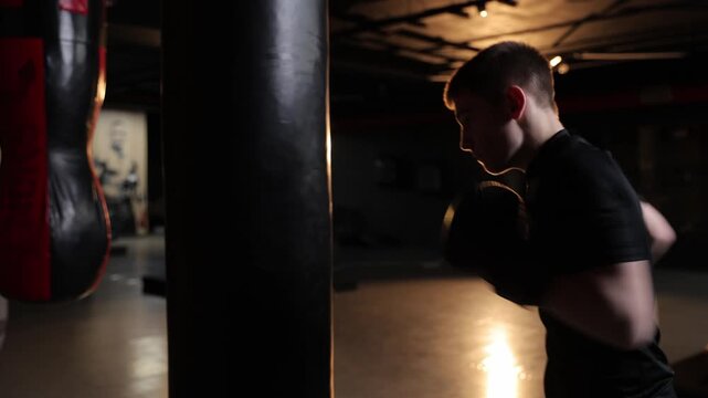 Young male boxer punching a heavy bag in a dark gym