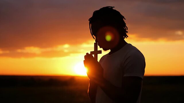Silhouette of a man holding a cross at sunset in contemplation