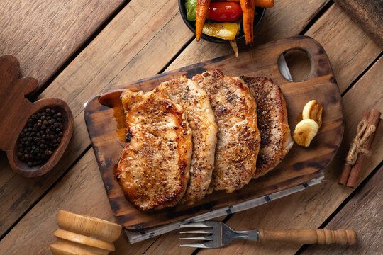 Top view of juicy grilled pork chops seasoned with black pepper on a rustic wooden cutting board.