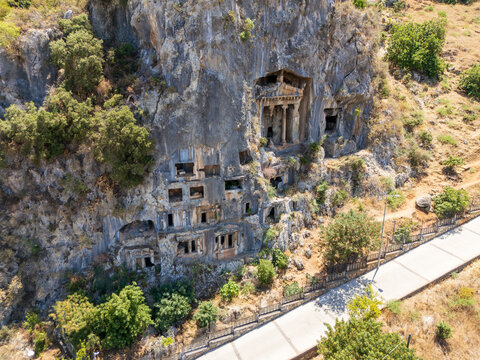 Fethiye, Turkey. Tomb of Amyntas, Ionic temple facade carved into a sheer cliff face, aerial view over ancient Lycian rock-cut tombs under bright summer sun