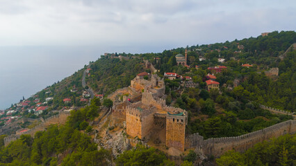 Obraz premium Alanya, Turkey. Aerial view of Alanya Bay in haze with fortress wall climbing mountain slope towards Ehmedek Castle in summer.. Aerial View