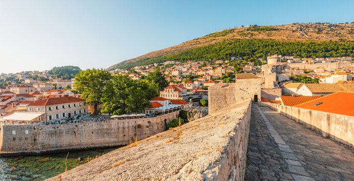 Golden hour panorama of Dubrovnik's historic fortifications and old port at dusk, featuring sunlight on ancient stone walls and Mediterranean architecture in Croatia