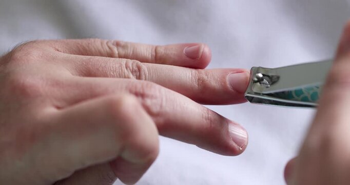 Man carefully trims his middle fingernail using metal clippers in home environment.