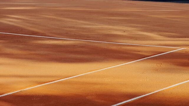 Empty clay tennis court with crisp white lines and warm sunlight, capturing clean sports geometry and the quiet atmosphere before play.