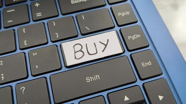 Closeup of finger press, push or click key with buy word lettering written on laptop computer keyboard. Stock market, share trading, online shopping, data purchase and ecommerce business concept.