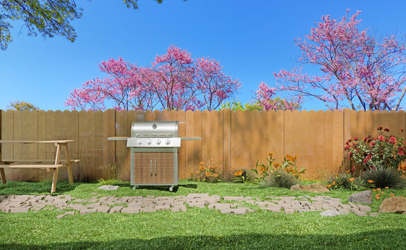 Backyard barbecue grill near wooden fence and blooming spring trees