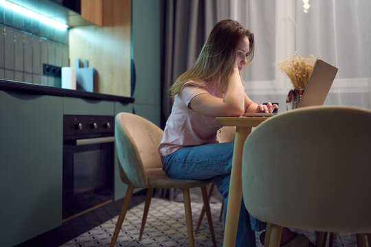 Freelance woman typing on laptop at night in modern home kitchen