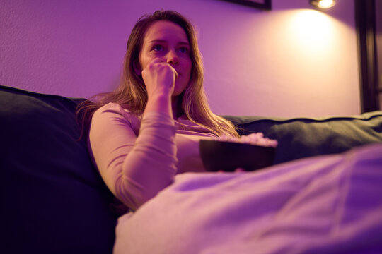 Female on sofa watching screen and eating popcorn indoors