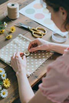Vertical shot of young adult woman arranging button on fabric swatch at craft table, creating handmade textile sample. Supporting sewing, DIY branding, artisan shop marketing