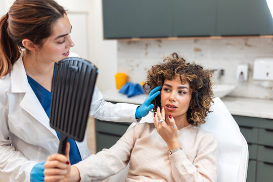 Smiling female patient holding mirror and looking at her face after beauty injection. Doctor showing results of cosmetic treatment, botox, dermal filler, plastic surgery and skincare concept.