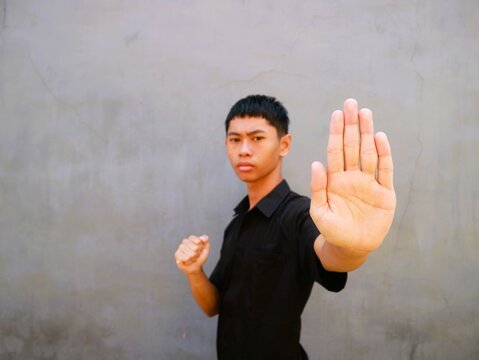 Young Asian man with short hair standing in a defensive stance against a gray wall