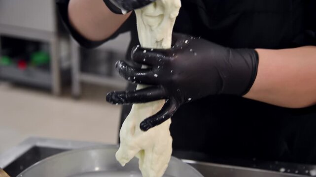 Making stracciatella cheese by stretching and kneading fresh curds in kitchen