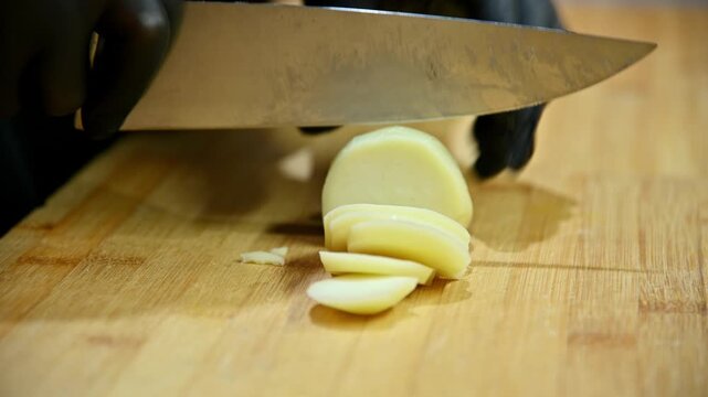 Chef slices potatoes with knife on wooden cutting board in kitchen setting