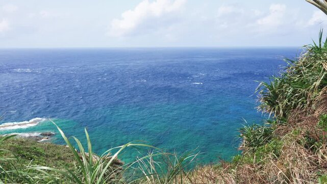 Vast blue ocean stretching to the west from the westernmost point of Japan, Yonaguni Island, Okinawa. Sunny day with rough waves and strong wind swaying coastal plants.