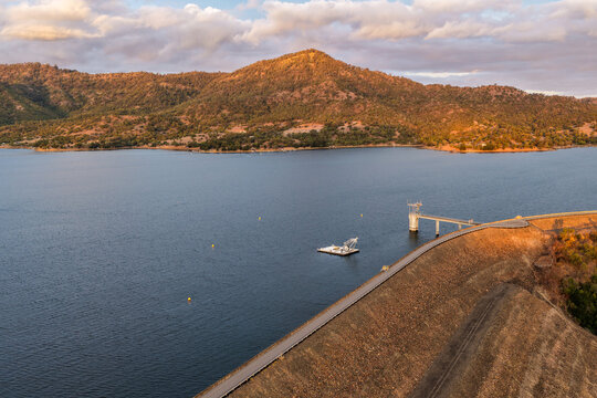 Aerial view of the Glenbawn Dam wall featuring the water intake system and servicing pontoon in NSW Australia. Drone photograph captures the engineering infrastructure, reservoir waters and landscape