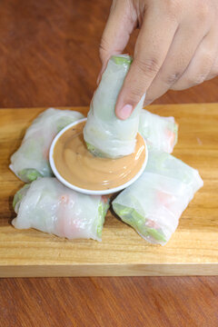 Close up of hand dipping fresh Vietnamese spring roll into peanut sauce