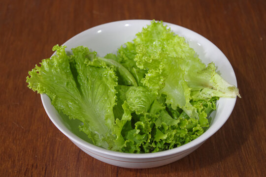 Fresh green leaf lettuce in white ceramic bowl on wooden table