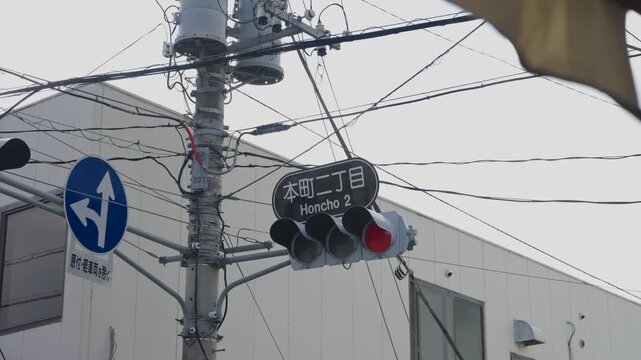Red traffic signal with Japanese street name sign and chaotic overhead cables at urban crossing