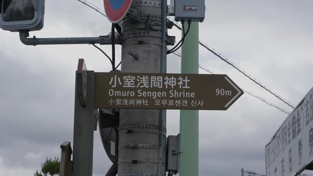 Brown directional signpost in Japanese Korean and English pointing toward shrine 90m away