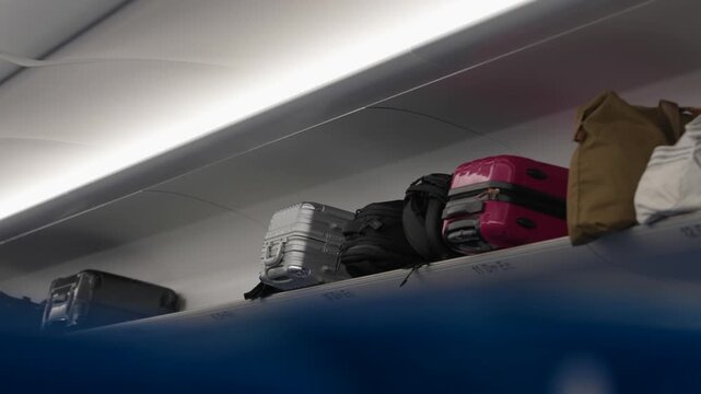 Travel bags and suitcases stacked on overhead shelf above seats inside high speed train