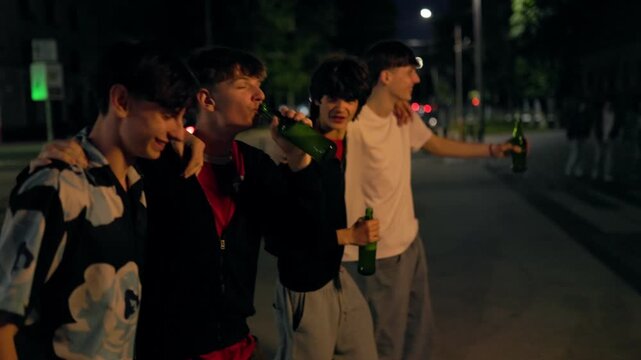 Four excited teenage boys shouting and drinking beer on a city street at night.