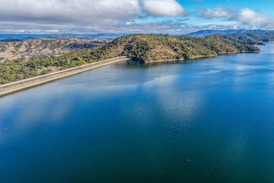 Aerial view of Glenbawn Dam and the dam wall leading towards the surrounding mountains in NSW Australia. Drone photograph captures the expansive reservoir, rugged inland landscape