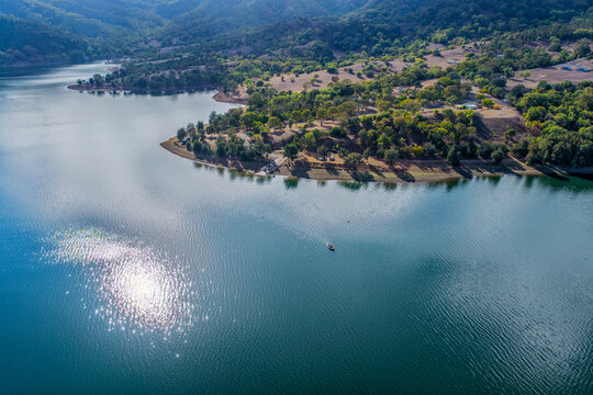 Aerial view of the Glenbawn Dam boat ramp and surrounding mountains with sunlight reflecting off the water in NSW Australia. Drone photograph captures the expansive reservoir, rugged inland landscape