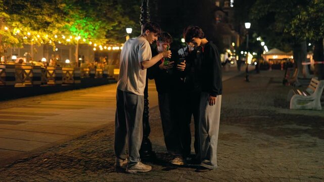 Wide shot of four teenage boys looking at a phone on a city sidewalk.