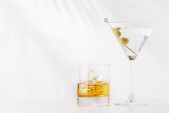 Glass of whiskey with ice and martini with olives on white background