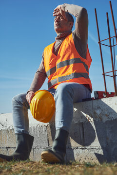 Construction worker having a heatstroke on a hot sunny day, headache, issues on a construction site outdoors.