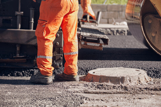 Construction workers working on a new asphalt layer on a public street.