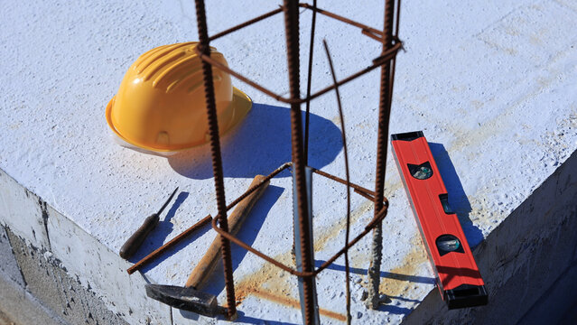 Construction tools and helmet on a cement foundation with iron rebar.
