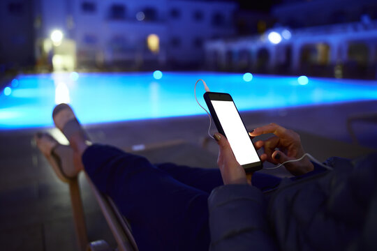 Woman using smartphone by pool at night &ndash; glowing screen, copy space, modern lifestyle