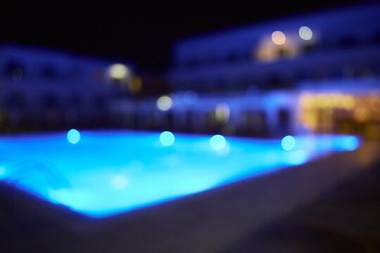 Glowing swimming pool in a luxury resort at night with blue illuminated water and soft background blur.
