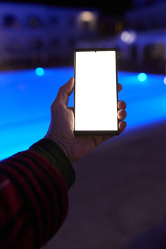 Woman using smartphone by pool at night &ndash; glowing screen, copy space, modern lifestyle