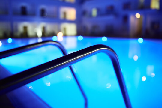 Glowing swimming pool in a luxury resort at night with blue illuminated water and soft background blur.
