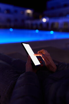 Woman using smartphone by pool at night &ndash; glowing screen, copy space, modern lifestyle