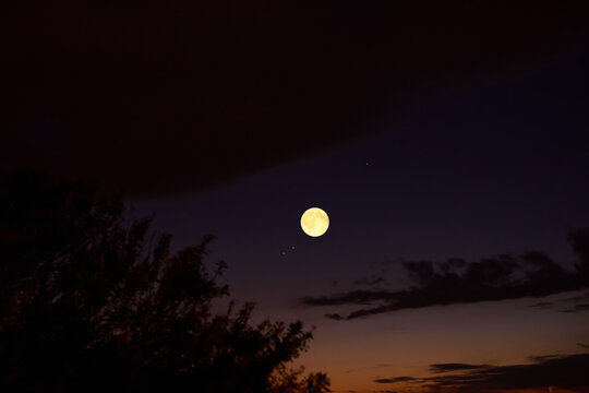 Full Moon on a twilight sky with landscape silhouettes.