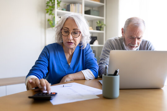 Senior couple managing domestic finances with laptop and calculator at home