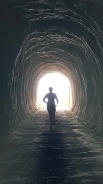 Vertical video. Silhouette of Woman Running Toward Bright Light at the End of Dark Tunnel, Cinematic Foggy Underground Passage, Personal Growth and Overcoming Depression