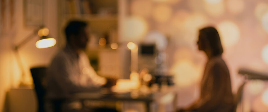 A softly focused image of a professional setting with two individuals engaged in conversation. The warm lighting creates a cozy atmosphere suitable for discussions.