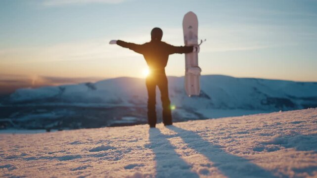 Summit conqueror, female snowboarder admiring view from mount top, back view. Happy woman lifting hands up when watching beautiful panorama with mountains range, enjoying freedom and beauty of nature