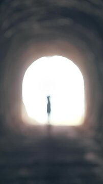 Vertical video. Silhouette of Woman Running Out of Bright Light Into Dark Tunnel, Cinematic Foggy Underground Scene About Entering the Unknown and Life Transformation
