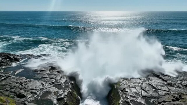 Epic ocean wave crashing through a narrow rock chasm creating a beautiful, powerful waterspout on a sunny day