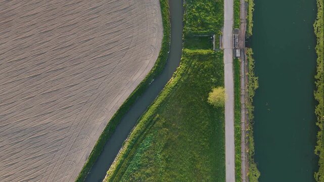 Naviglio di Cremona in Cremona Lombardy Italy flows alongside narrow irrigation canal and farm track within Po Valley agricultural grid showing water management layout, drone top down forward